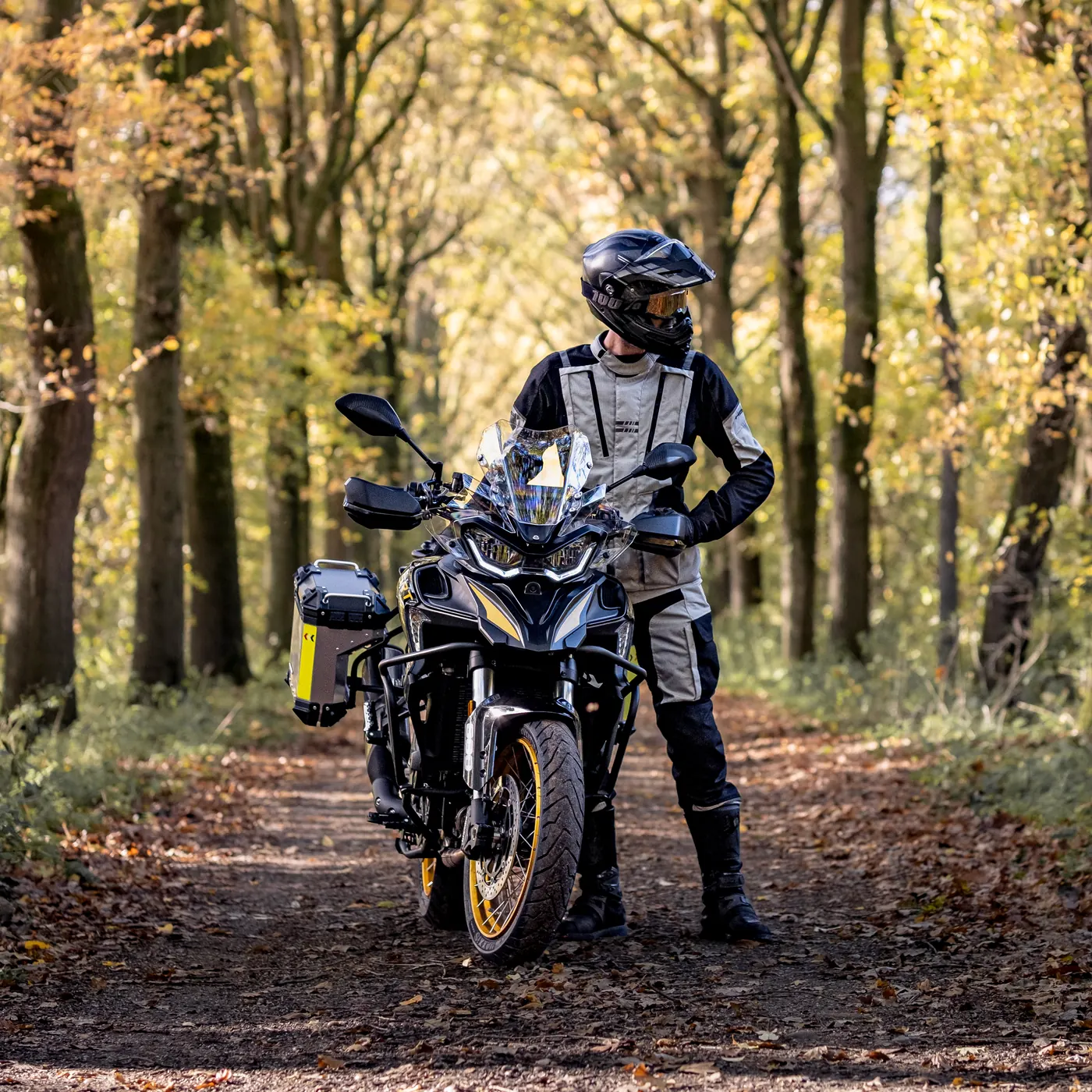 Rijder naast een QJMotor SRT 900 op een bospad in de herfst